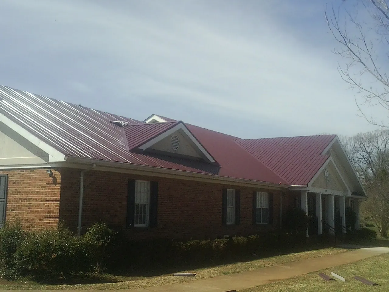 Red metal roof with gabled entries on a long brick building, from a Hail Damage Roof Repair job in Bishopville