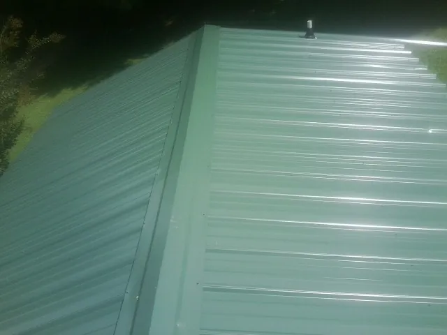 New green metal panels meeting at the ridge of a roof — Flat Roof Repair work by our crew in Bishopville