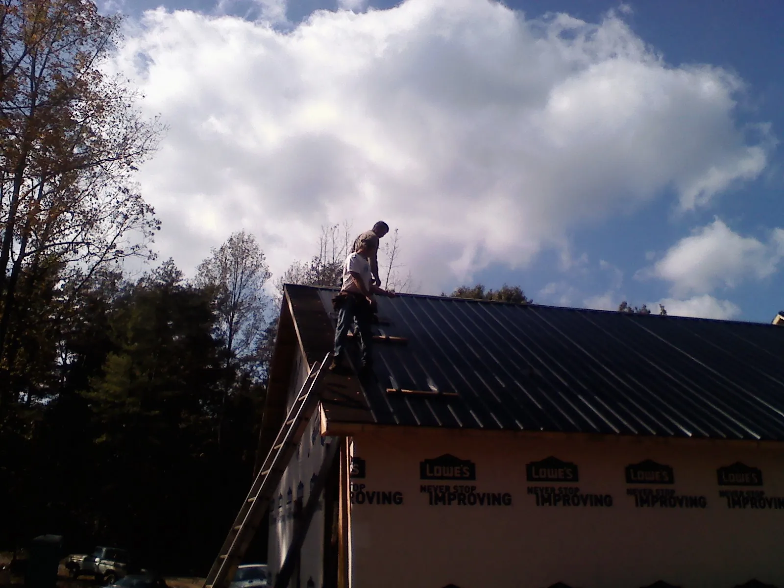 Roofer fastening dark metal panels high against a cloudy sky, from a Roof Inspection job in Bishopville